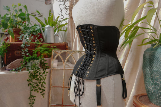 A black training corset with gold hardware on a mannequin