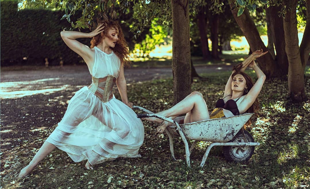 Two models wear ribbon corsets, one in a wheelbarrow