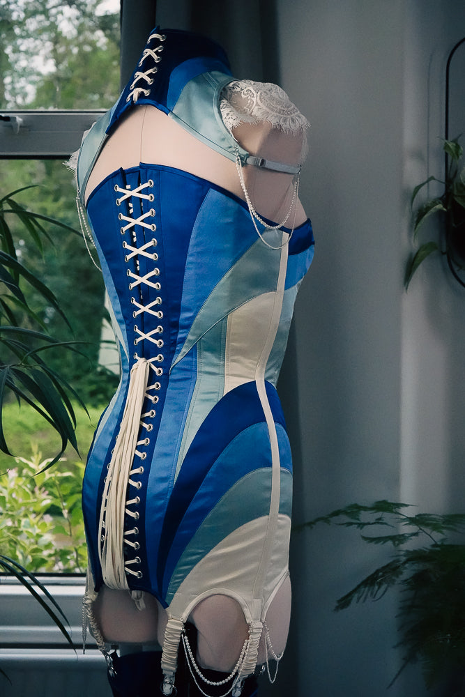 A blue and ivory corset dress on a mannequin with matching posture capelet and pearl details.