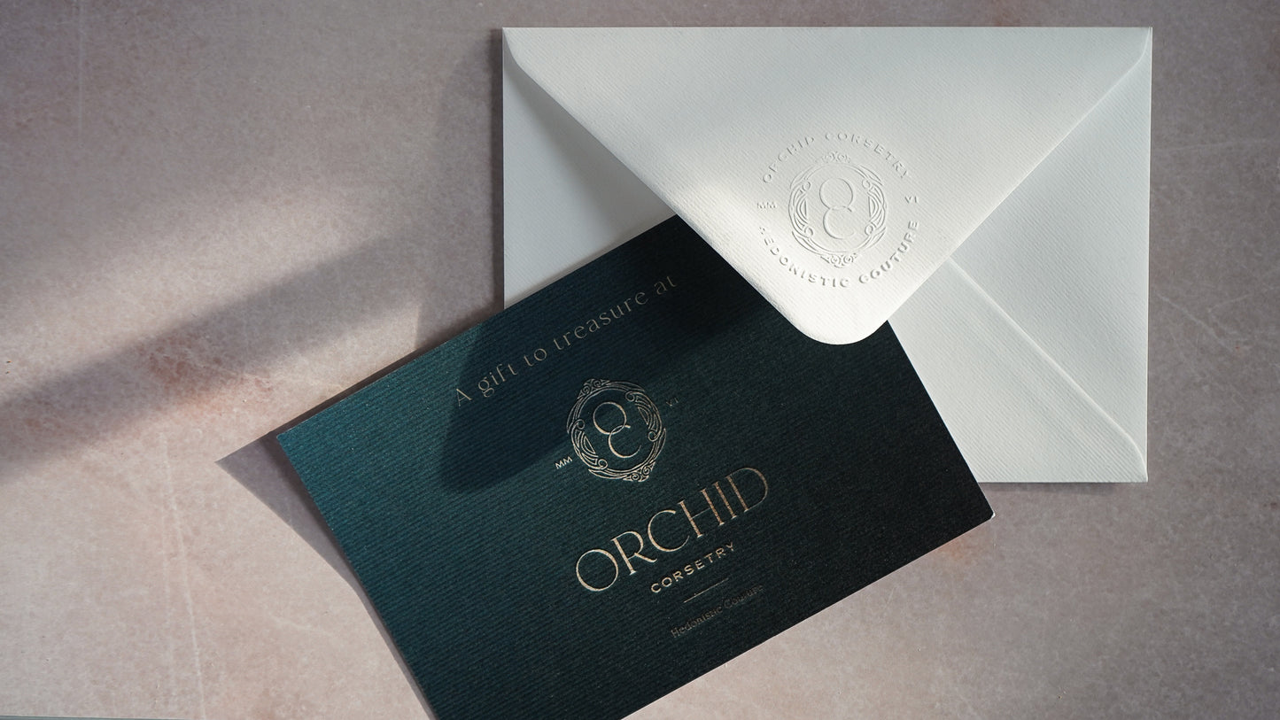 A teal and gold gift card for Orchid Corsetry with an embossed envelope.